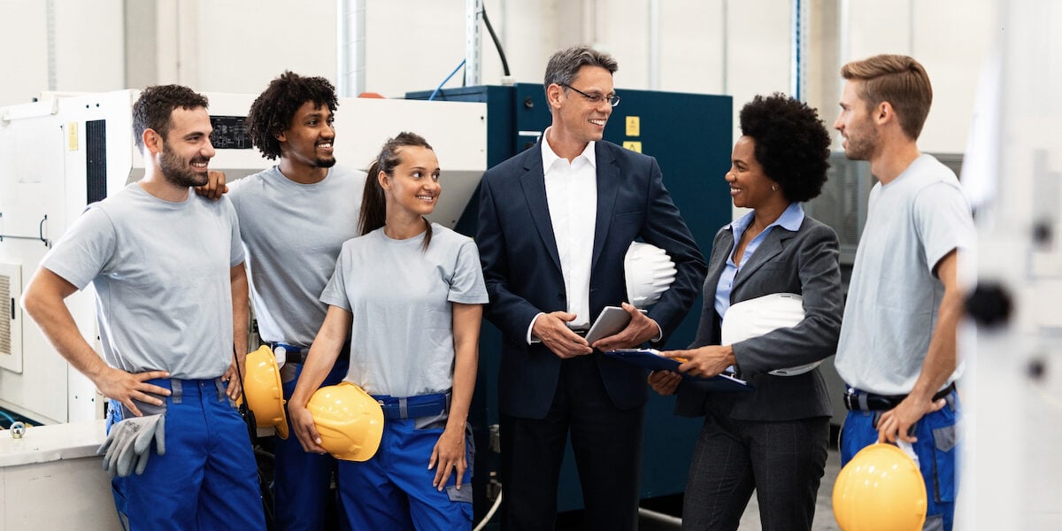 Group of happy workers talking with company leaders in a factory.
